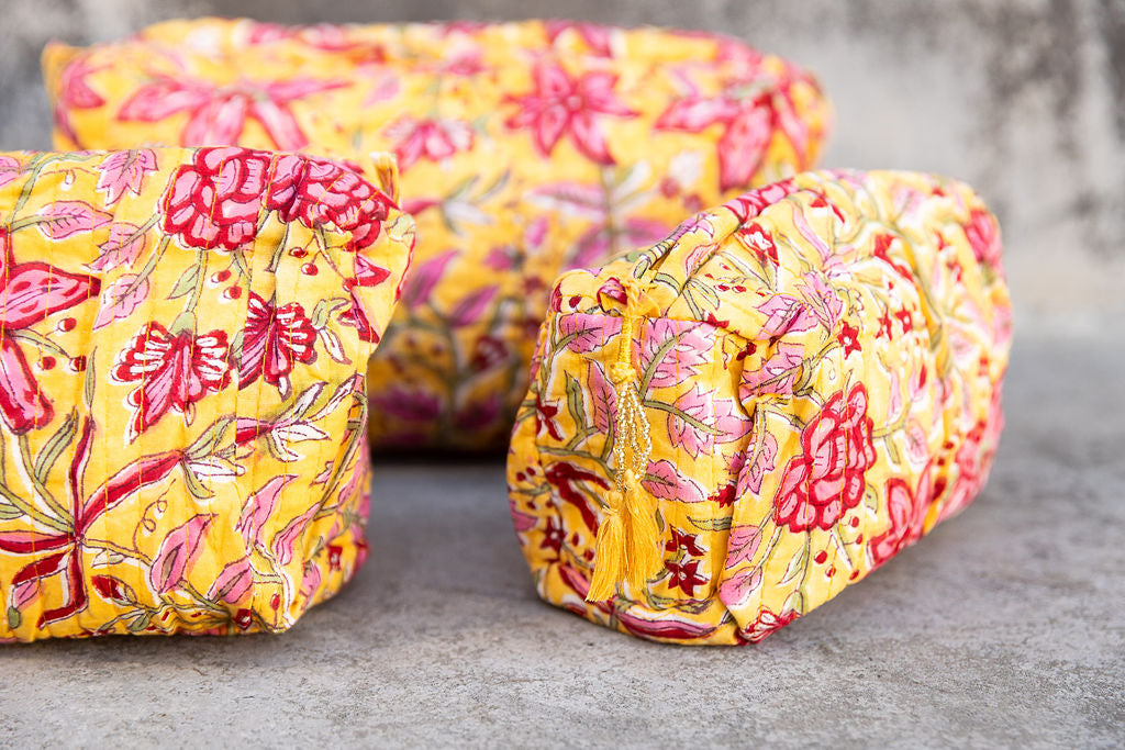 Set of three multi-colored patterned cotton cosmetic bags. Smaller bags fit into the largest for easy storage. Red and pink floral on yellow. Detail