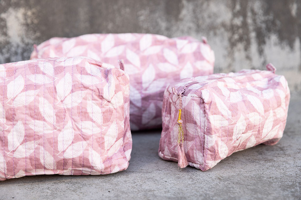 Set of three multi-colored patterned cotton cosmetic bags. Smaller bags fit into the largest for easy storage. Leaf pattern on pink. Detail.