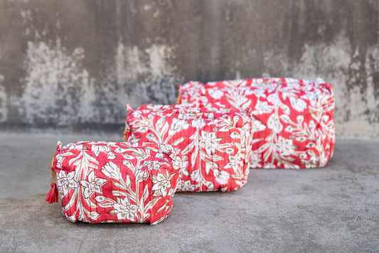 Set of three multi-colored patterned cotton cosmetic bags. Smaller bags fit into the largest for easy storage. White floral on red.