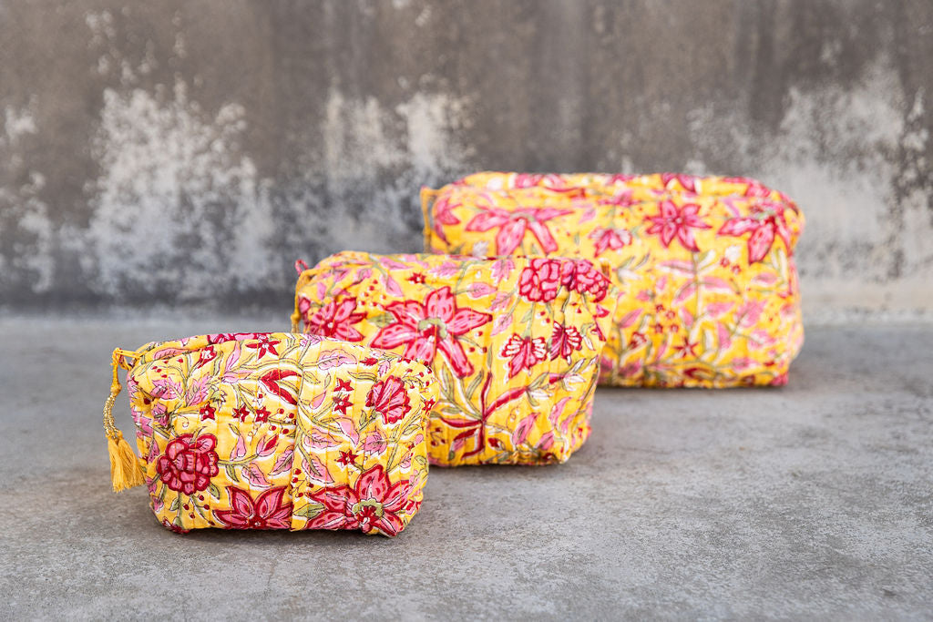 Set of three multi-colored patterned cotton cosmetic bags. Smaller bags fit into the largest for easy storage. Red and pink floral on yellow.