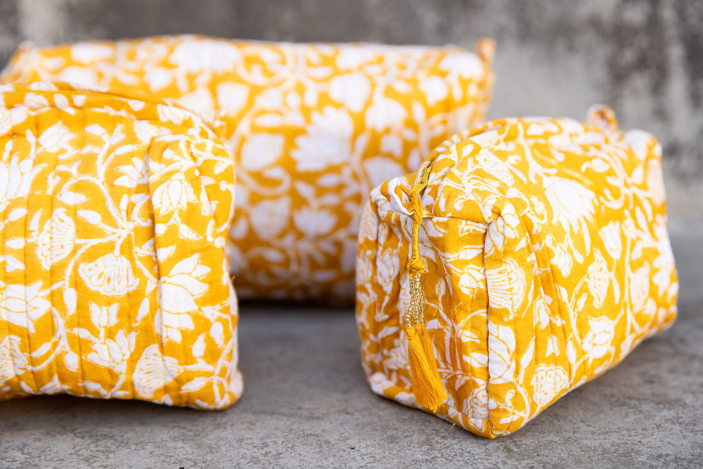 Set of three multi-colored patterned cotton cosmetic bags. Smaller bags fit into the largest for easy storage. White coral pattern on yellow. Detail.