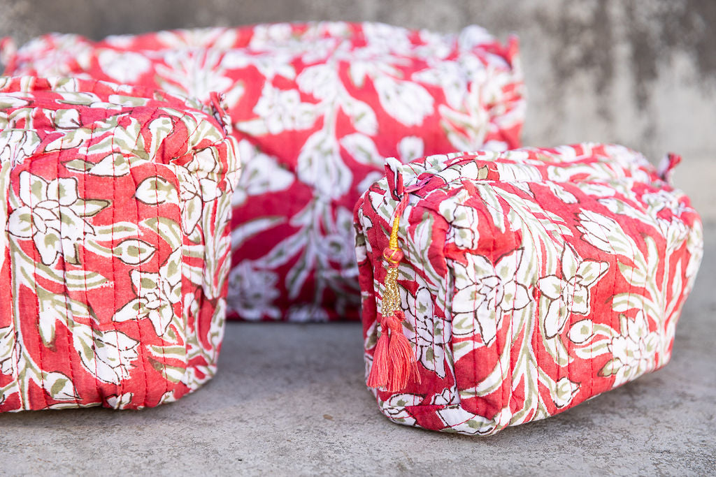 Set of three multi-colored patterned cotton cosmetic bags. Smaller bags fit into the largest for easy storage. White floral on red. Detail.